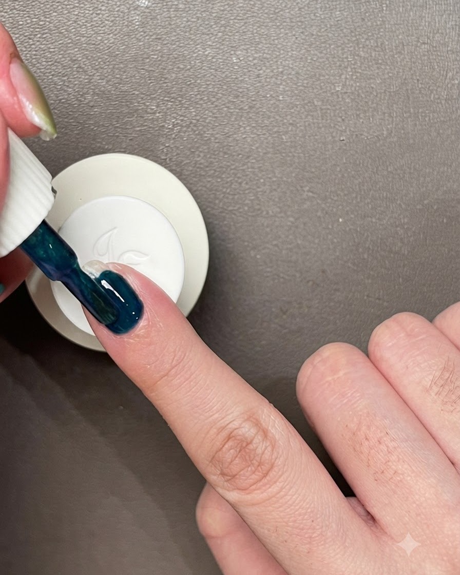 Aplicando una capa de esmalte de gel azul verdoso oscuro directamente sobre una uña natural sin esmalte.