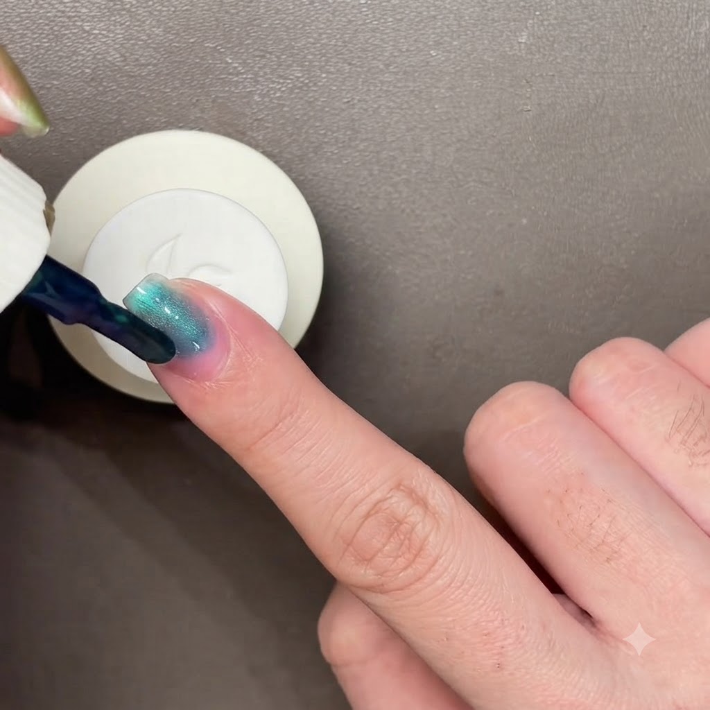 Una varita magnética negra flotando sobre una uña pintada de azul verdoso oscuro para manipular el esmalte ojo de gato.