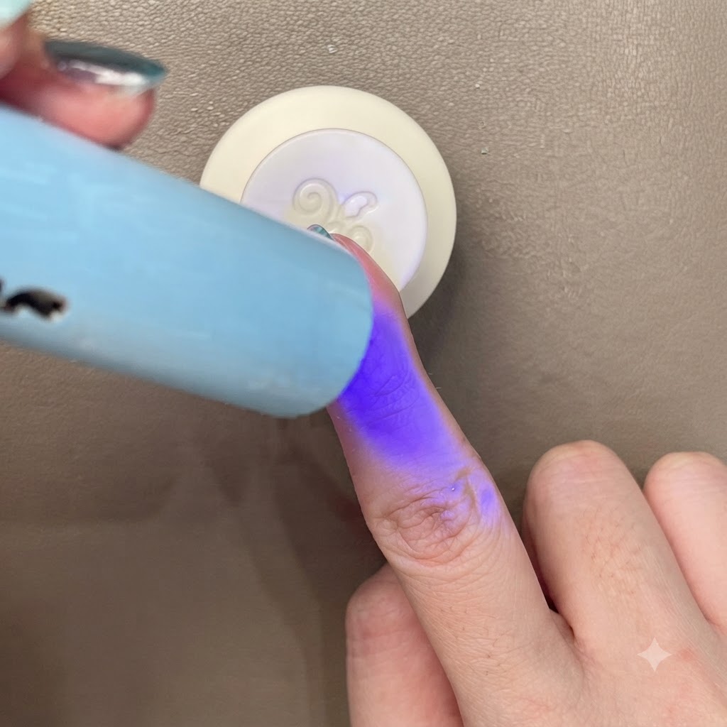 Curando una uña con efecto ojo de gato azul verdoso bajo una pequeña luz UV/LED azul portátil.