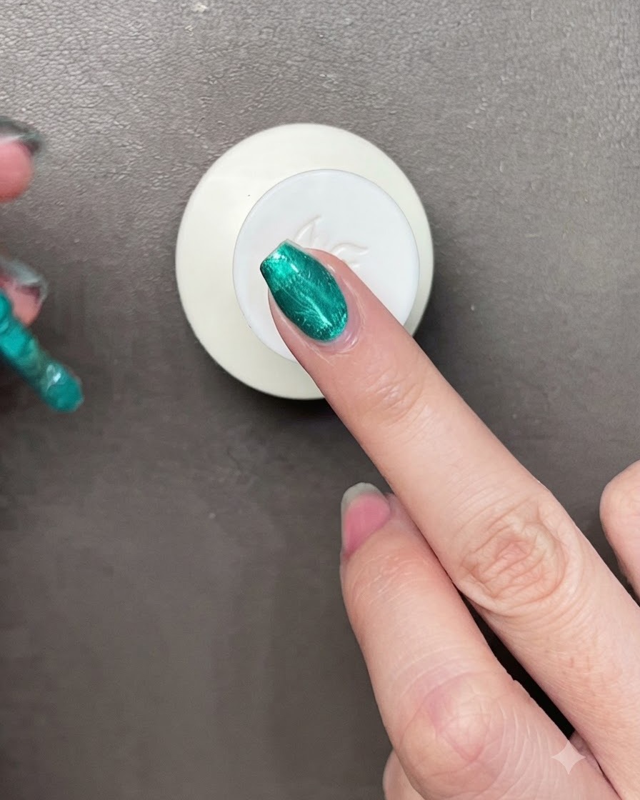 Un pincel aplicando esmalte de gel verde metálico vibrante sobre una uña con un pequeño imán visible cerca.