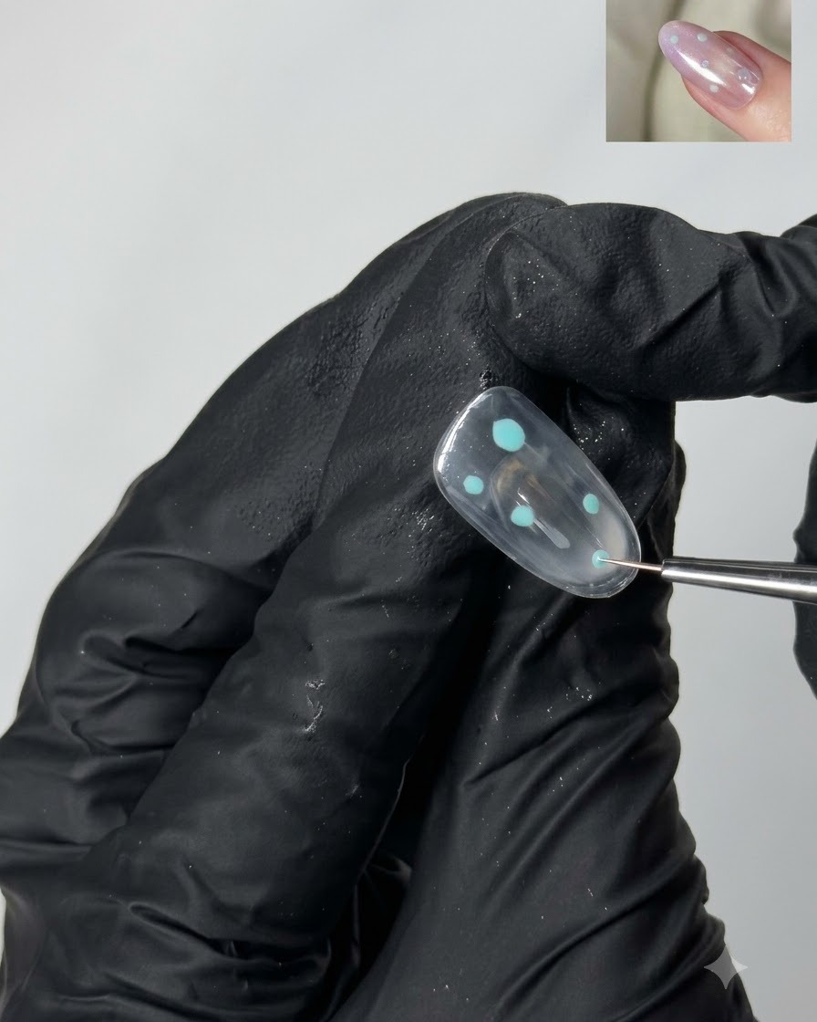 Un pincel de detalle fino colocando pequeños acentos de puntos turquesa sobre la superficie de una uña de gel transparente.