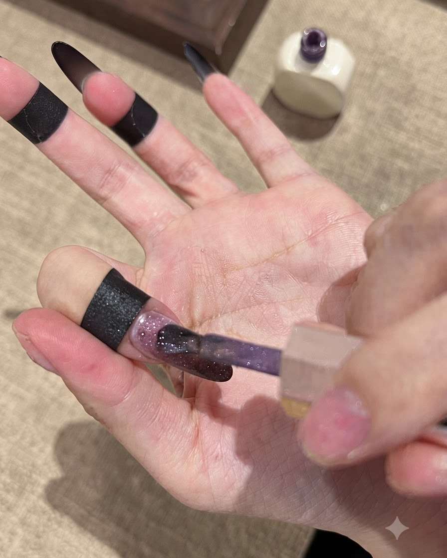 Un pincel aplicando esmalte en gel Fallen Gold Cat Eye sobre una base de uñas con degradado oscuro.