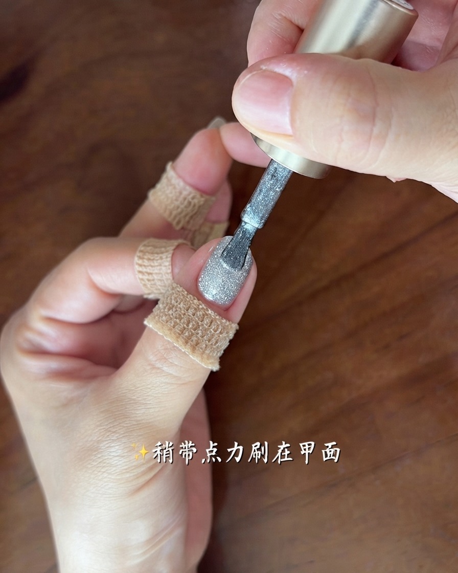 Un pincel aplicando una capa fina y brillante de gel ojo de gato gris plateado en una uña.