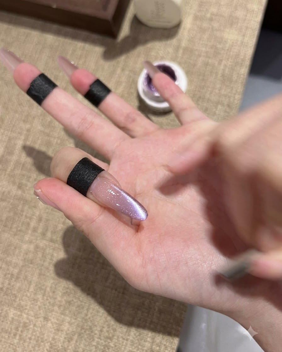 Primer plano de una uña almond alargada que muestra un esmalte de gel ojo de gato morado recién fijado con un centro brillante y reflectante.