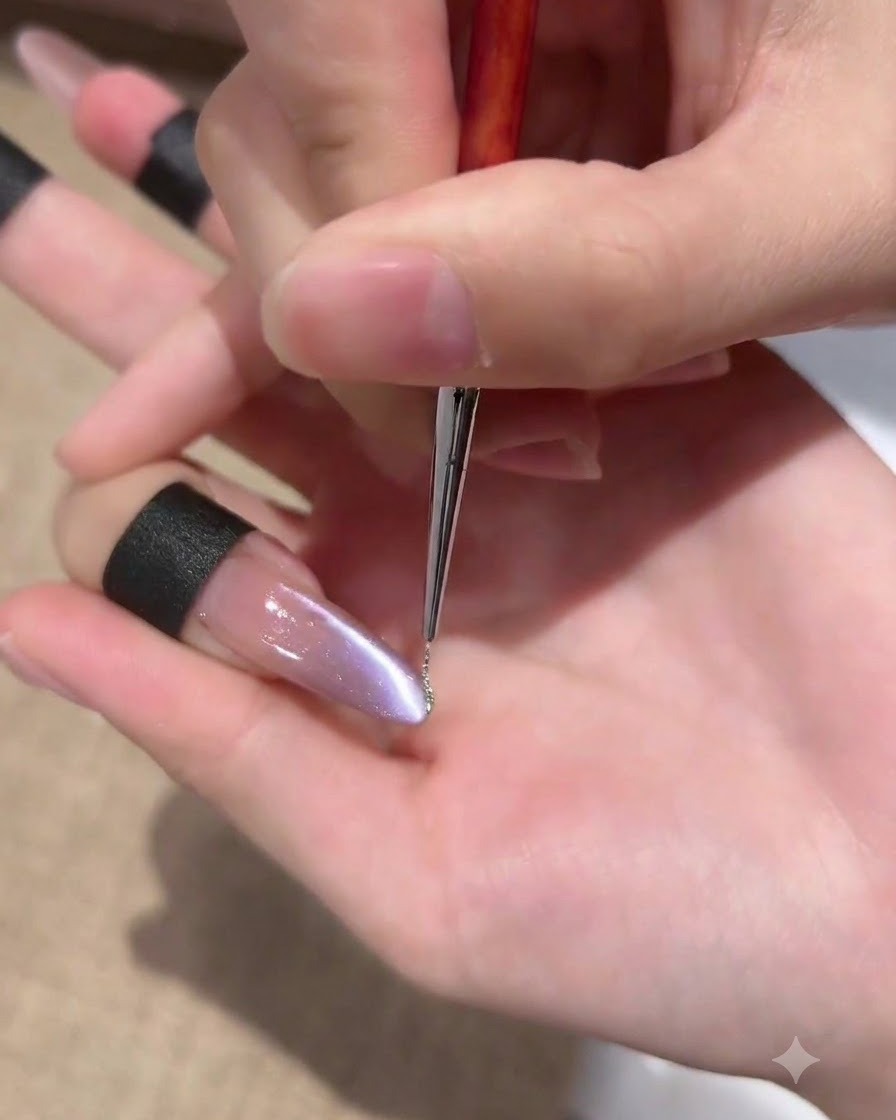 Un pincel delineador fino aplicando una línea muy fina de gel con purpurina plateada brillante a lo largo del lateral de una uña con efecto ojo de gato morado.