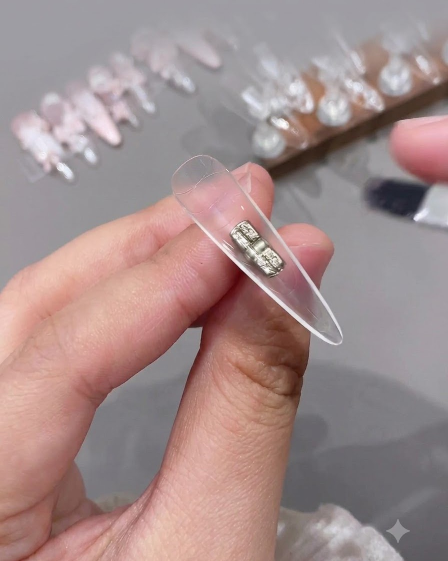 Pincel pequeño aplicando top coat transparente en la parte cóncava interior de un tip de uña artificial.