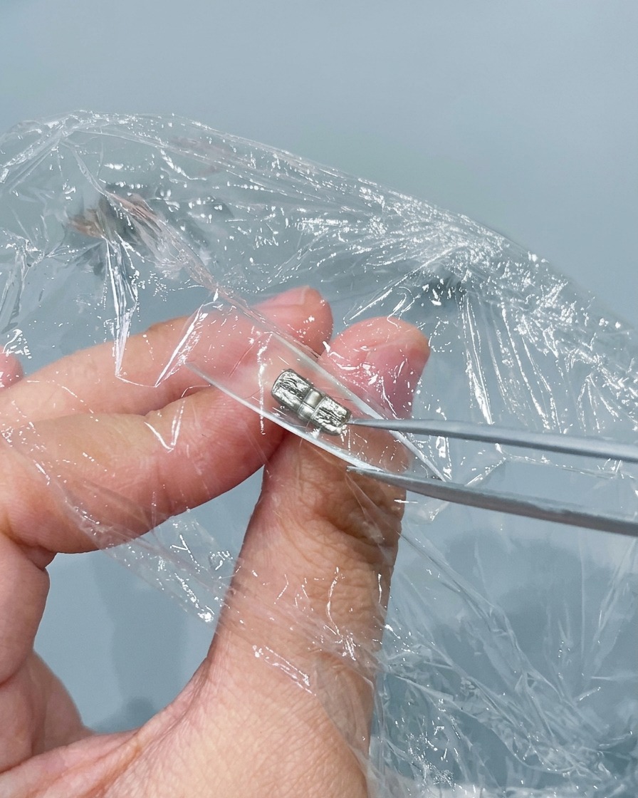 Pinzas de metal pellizcando y arrugando el papel film presionado dentro de un tip de uña transparente.