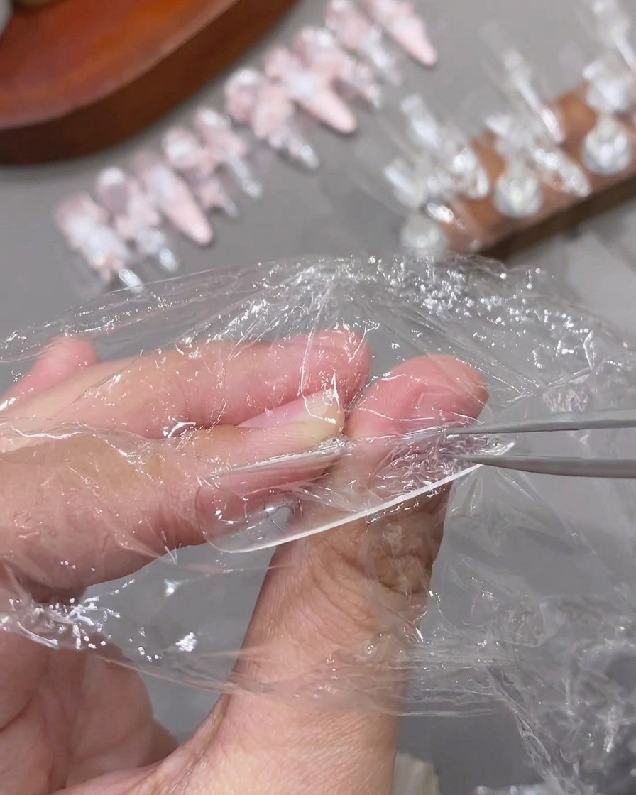 Pinzas despegando el papel film de un tip de uña transparente ya curado y texturizado.