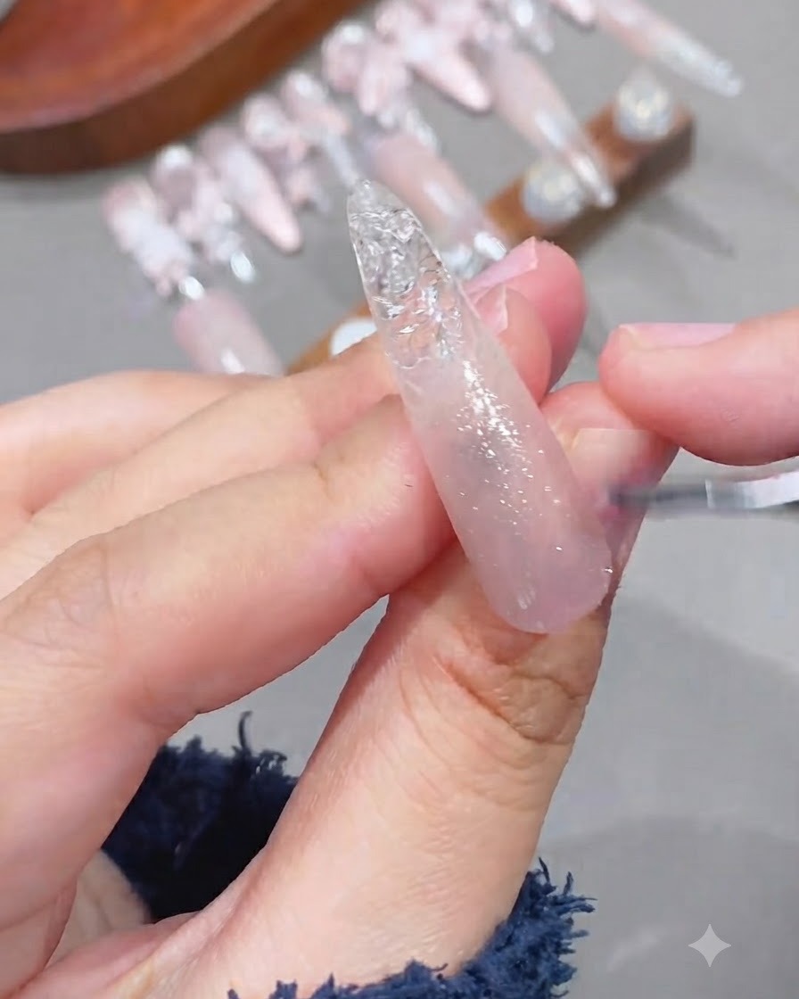 Primer plano de un pincel aplicando gel brillante de ojo de gato sobre una base de uña con degradado rosa.