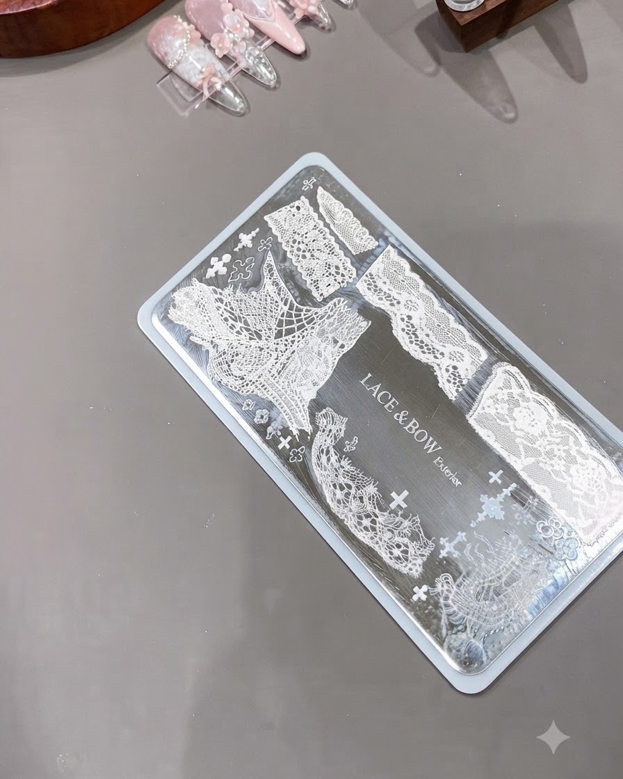 Estampador de uñas de silicona transparente posicionado junto a una placa de metal grabada que muestra intrincados patrones de encaje blanco.