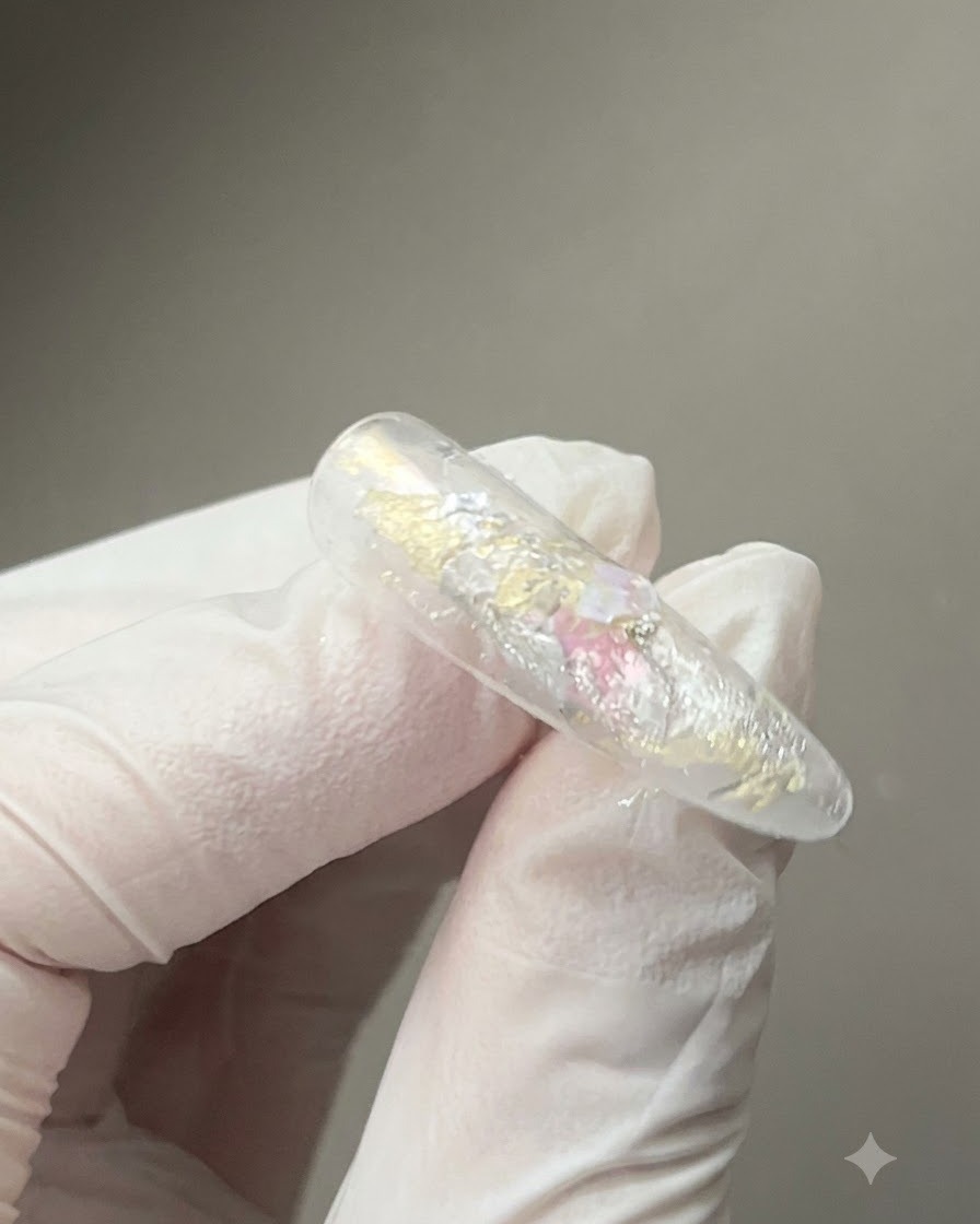 Una herramienta de imán sostenida de cerca sobre una uña recubierta de gel brillante para dar forma a las partículas magnéticas reflectantes ojo de gato.
