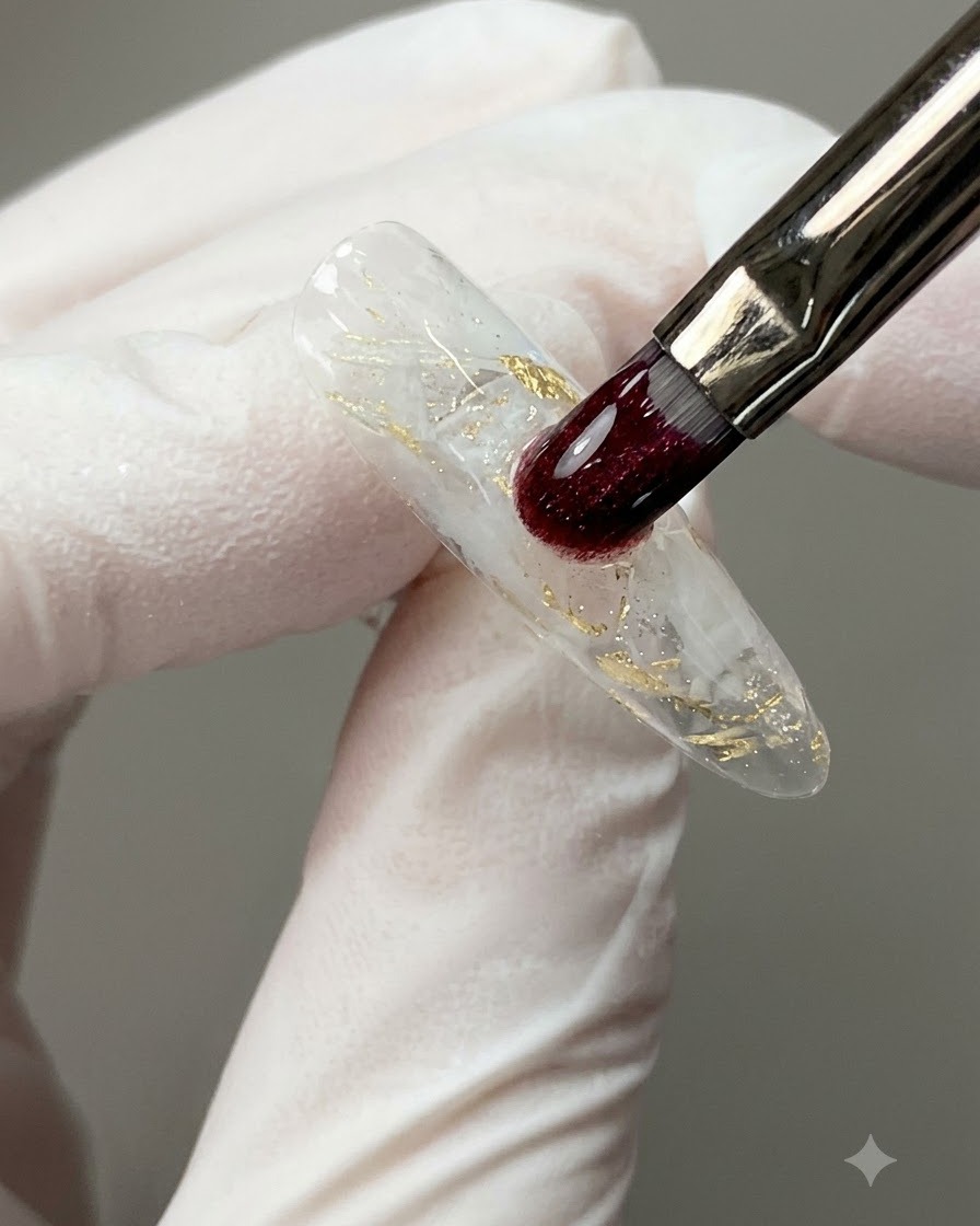 Un pincel de uñas aplicando una gota de nivelación clara de gel de construcción sobre una superficie de uña decorada.