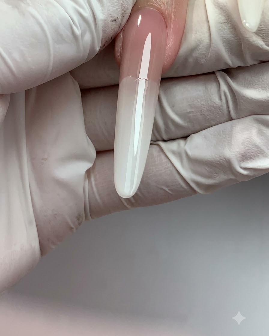 Una uña postiza larga que muestra una transición de degradado ombré suave desde el nude en la parte superior hasta el blanco lechoso en la punta.