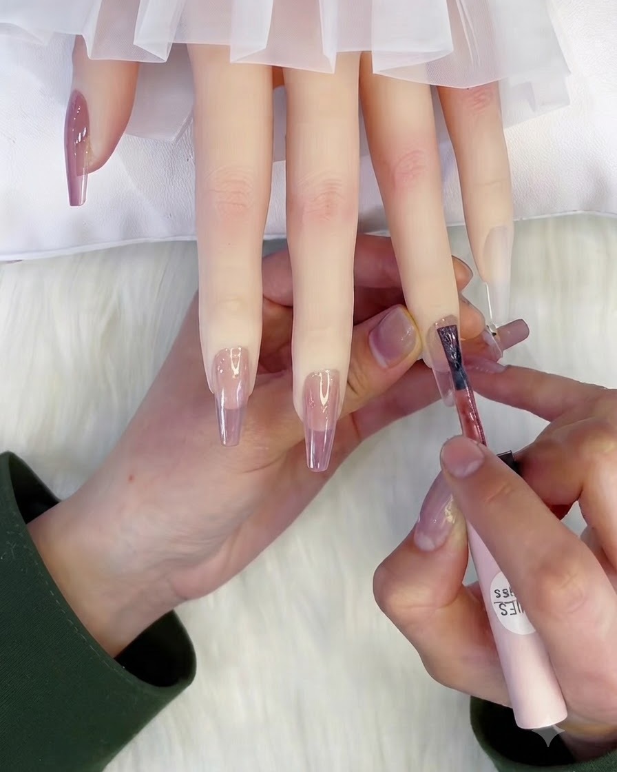 Un pincel aplicando una segunda capa de esmalte de gel rosa translúcido sobre una uña.