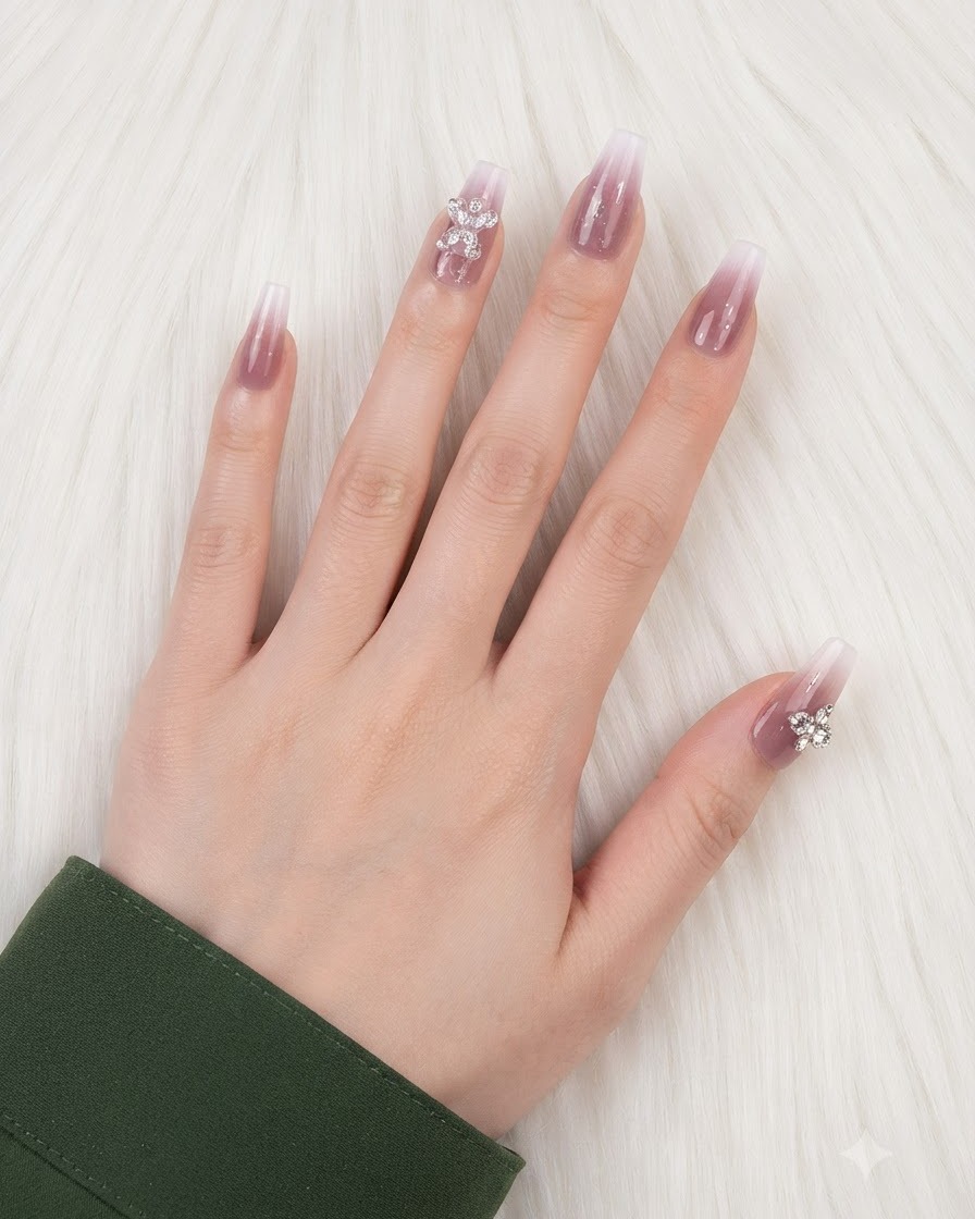 Una mano con uñas con degradado terminadas y abalorios colocados en el dedo anular y el pulgar.