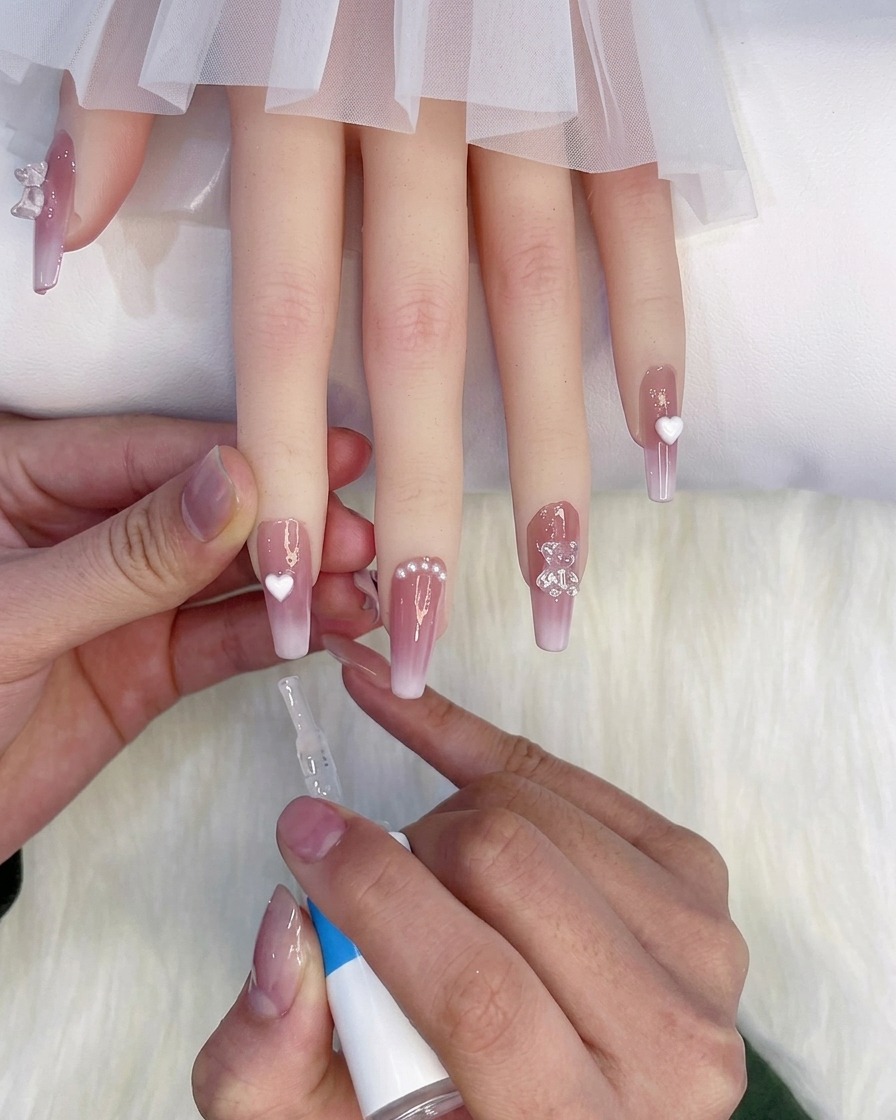 Un pincel de botella aplicando una capa superior brillante sobre los dedos con manicura apoyados sobre un fondo blanco suave.