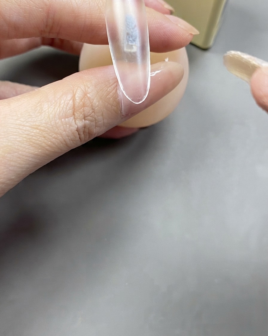 Un pincel aplicando una capa transparente de gel base sobre una extensión de uña transparente.