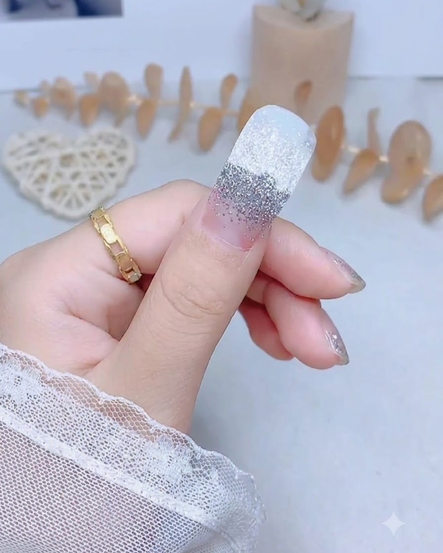 Una uña del pulgar con una pegatina de purpurina plateada siendo presionada firmemente por el centro.