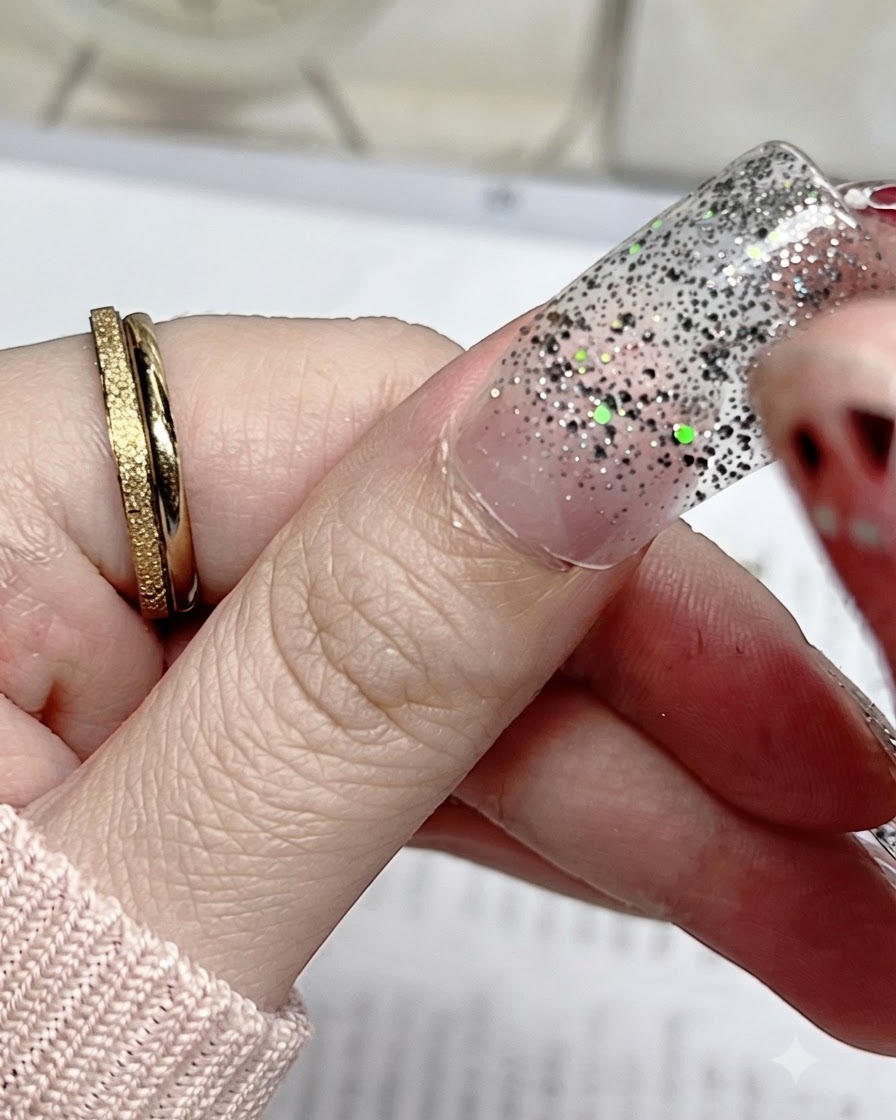 Un primer plano de una pegatina de uña con brillo plateado alineándose con precisión con la cutícula de una uña de pulgar natural.