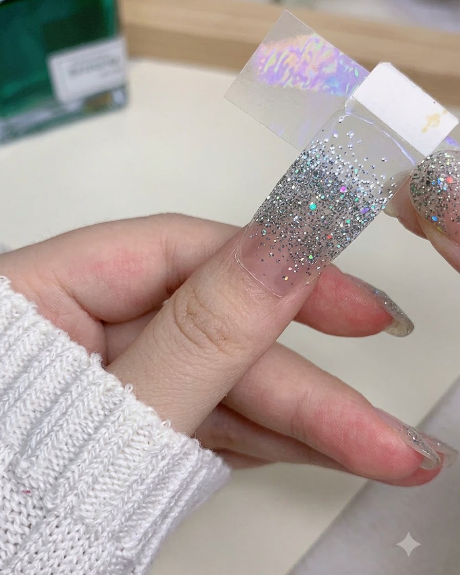 Un primer plano de una mano sosteniendo una extensión de uña postiza mientras usa cuidadosamente una herramienta para ajustar su borde.