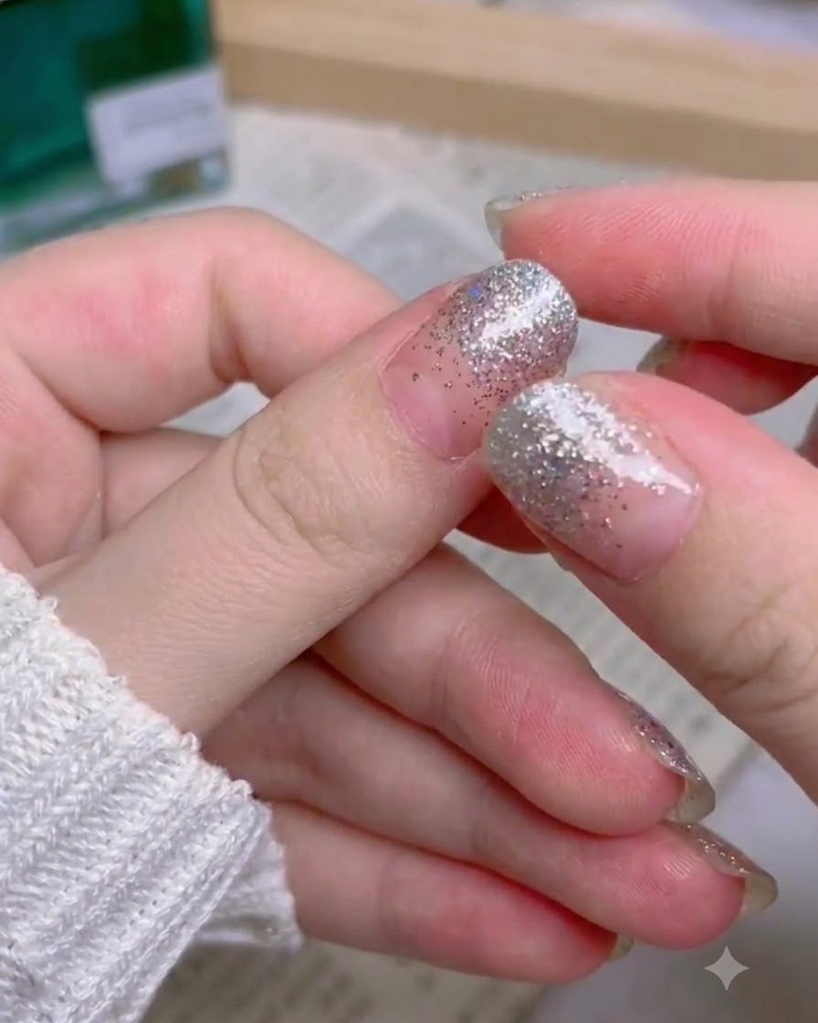 Una mano que muestra el conjunto completo terminado de uñas postizas con degradado de purpurina plateada.