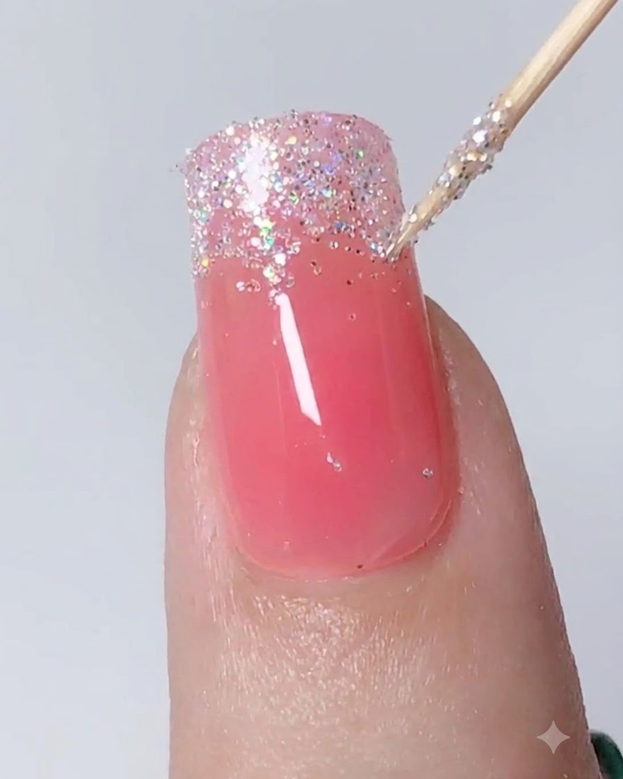 Una herramienta de detalle dando toques y estirando el glitter plateado hacia abajo para crear un degradado ombré en una uña.