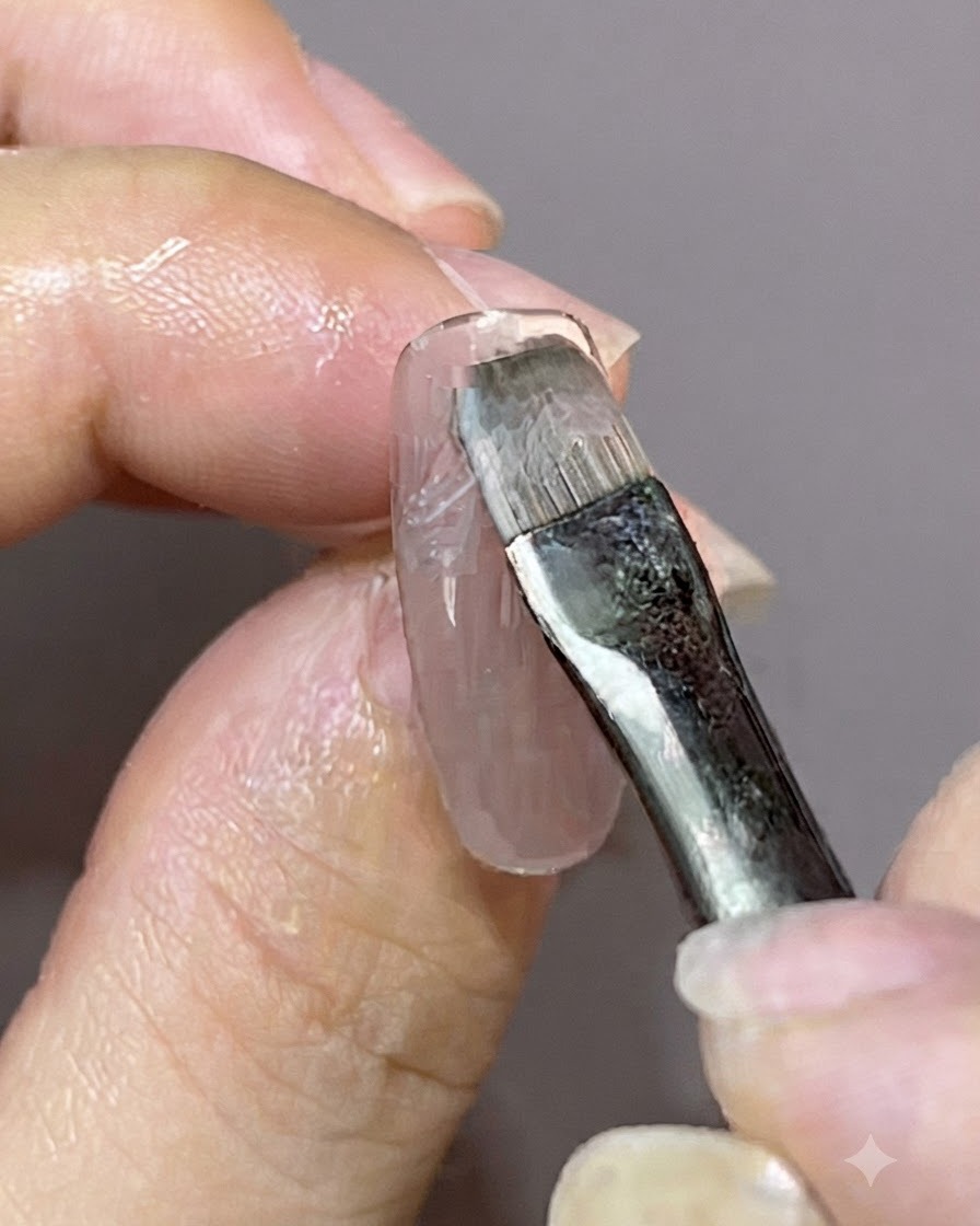 Un pincel de detalle aplicando una capa fresca de esmalte en gel sobre un diseño de uña magnética preexistente.