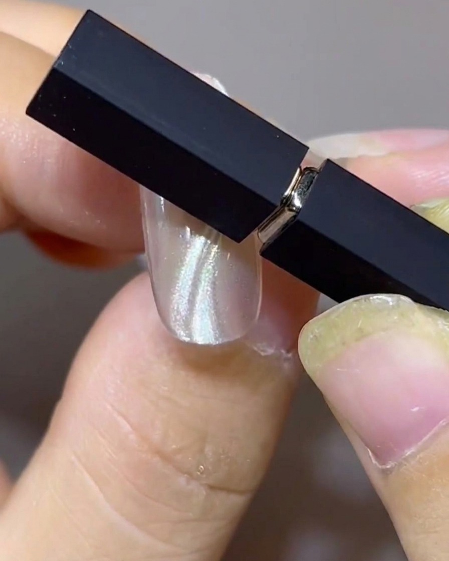 Dos imanes posicionados en un ángulo sobre una uña para dar forma a bandas cat-eye flotantes dobles y paralelas.