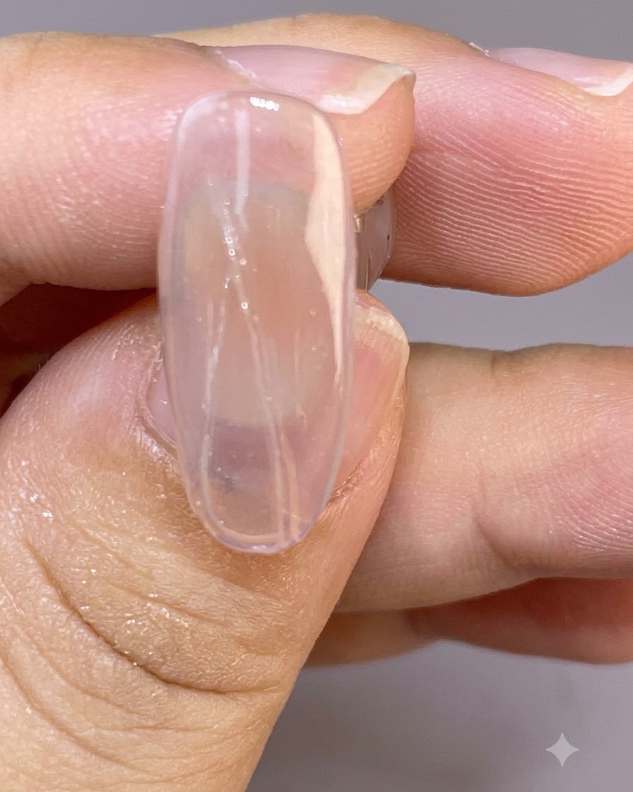 Un primer plano de una uña clara que muestra finas y delicadas líneas de plumas pintadas a través de la superficie húmeda.