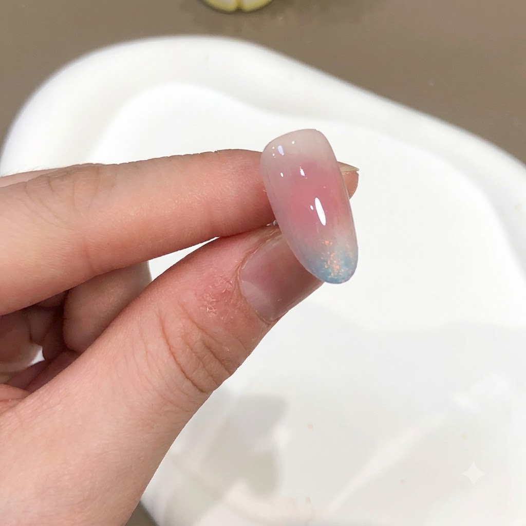 Primer plano de una uña mostrando un efecto de polvo aurora en tonos rosa y azul con un acabado de alto brillo.