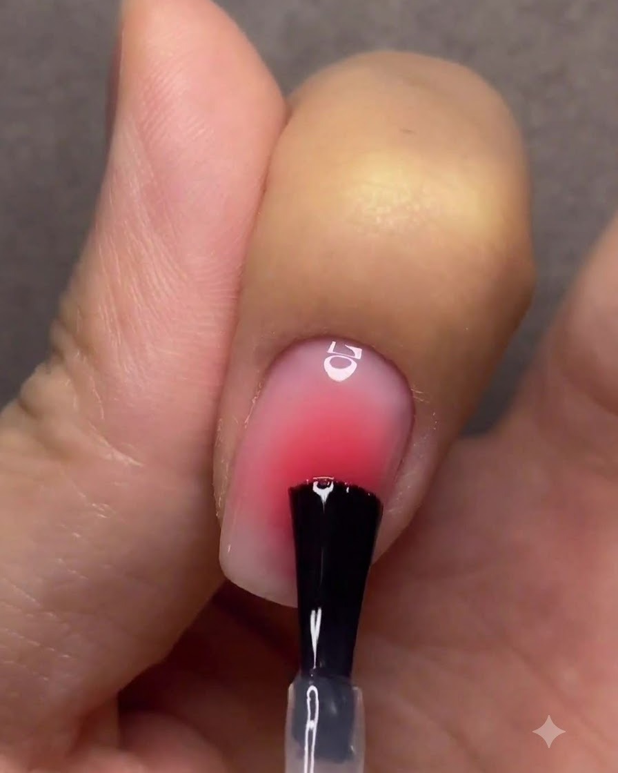 Una mano con uñas degradadas terminadas curando bajo una lámpara de uñas UV o LED rosa.
