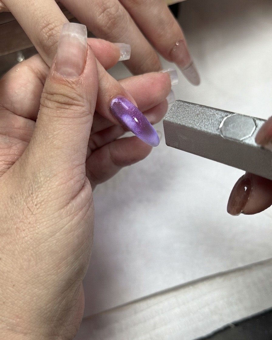 Una varita magnética utilizada sobre un bloque de color morado con efecto ojo de gato aplicado en un dedo índice.