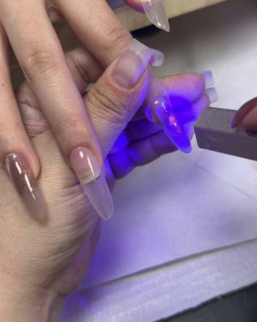 Una luz UV curando una uña pintada mientras otros dedos con gel ojo de gato en degradado descansan cerca.
