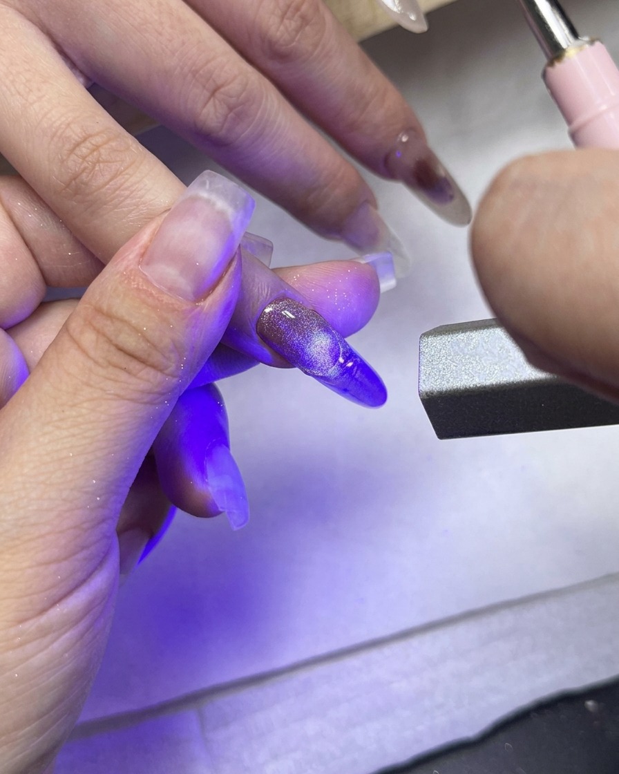 Una luz de curado UV/LED apuntando directamente al dedo medio mostrando la punta francesa texturizada.