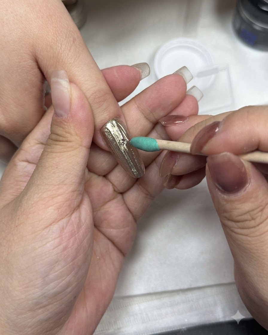 Un pincel de manicura aplicando top coat sobre una superficie de uña con acabado cromado.