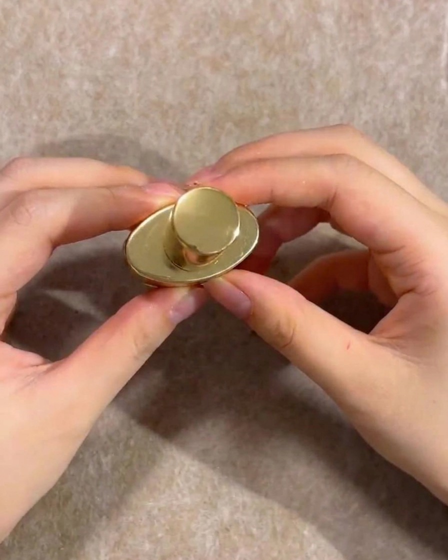 Manos sosteniendo el tapón dorado de un frasco de esmalte de gel nude.