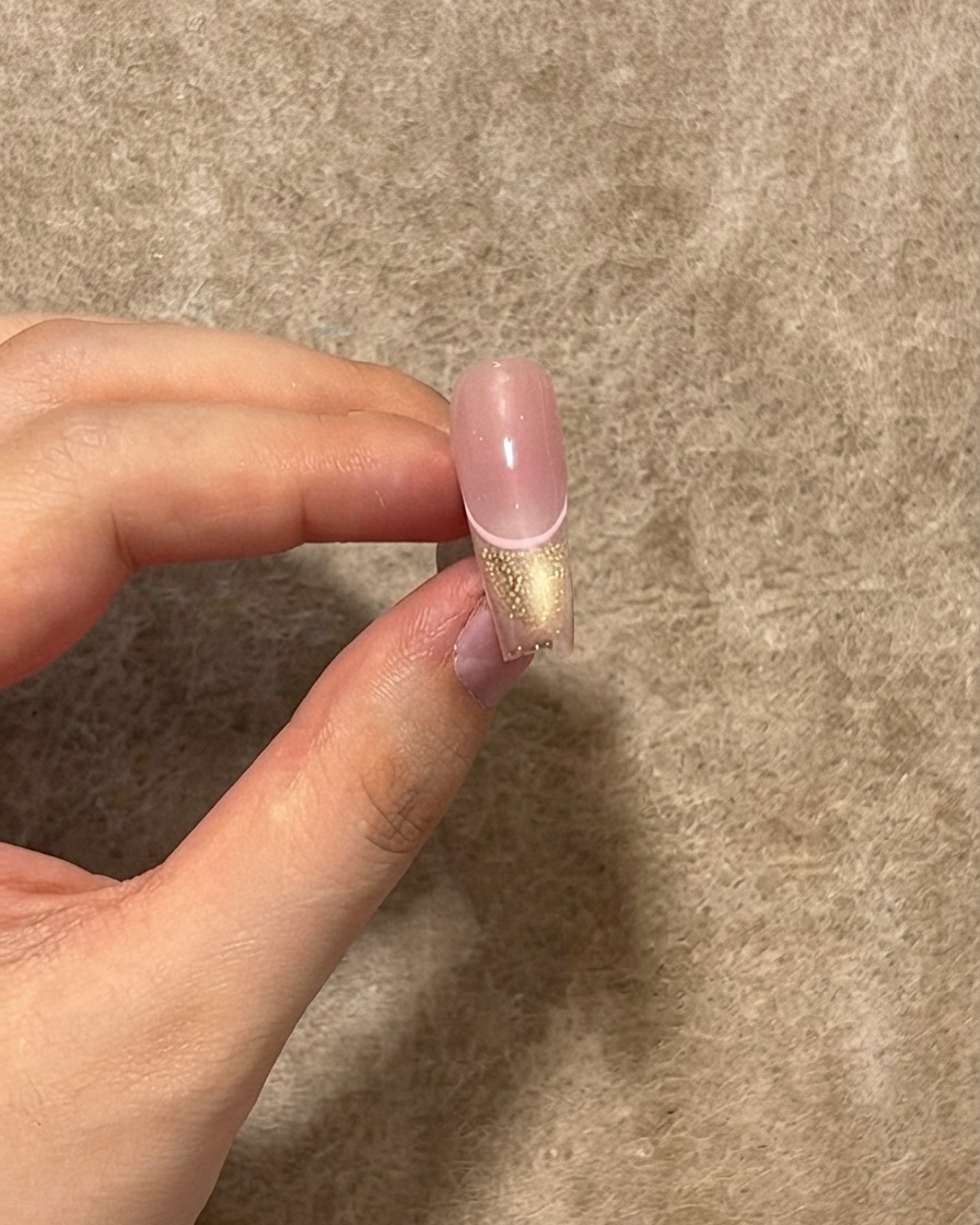 Una uña terminada que muestra una capa de top coat brillante aplicada sobre la línea rosa, la punta cat eye y el centro rubor.
