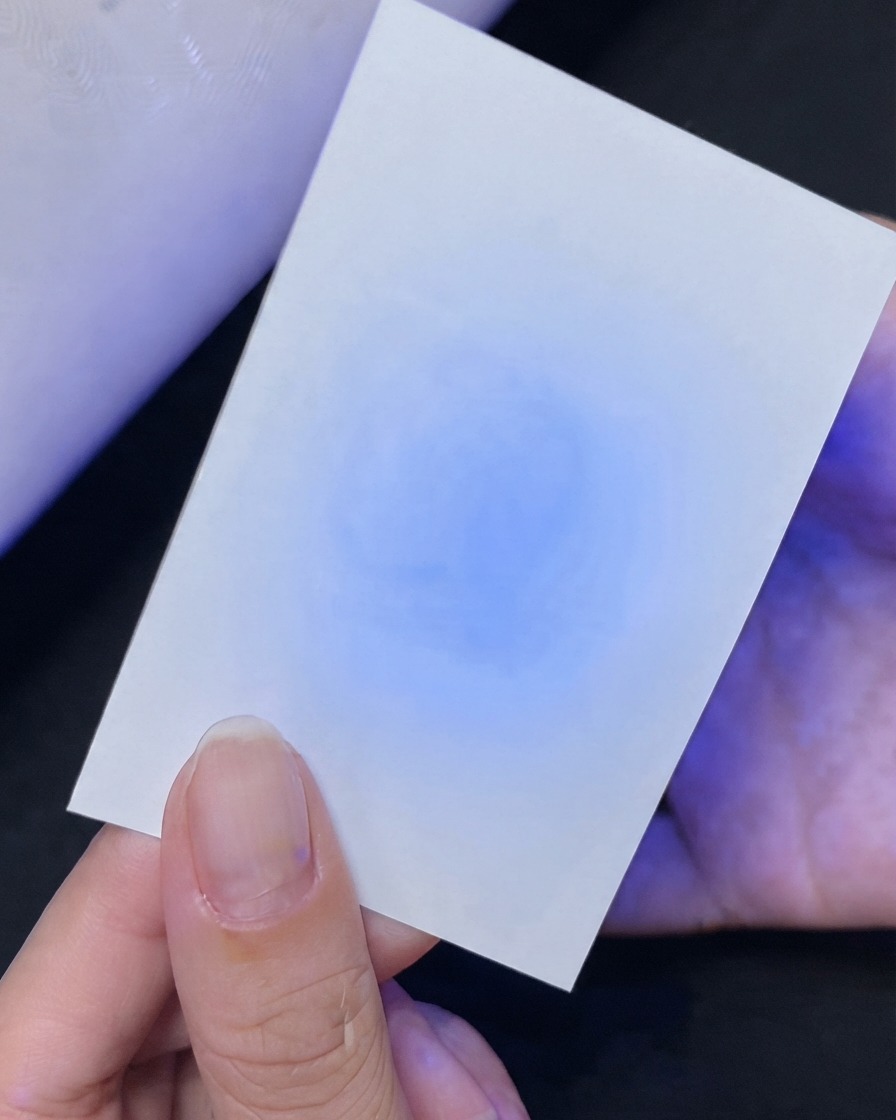 Una mano sosteniendo una tarjeta blanca que muestra una prueba de reflexión de luz UV azul debajo.