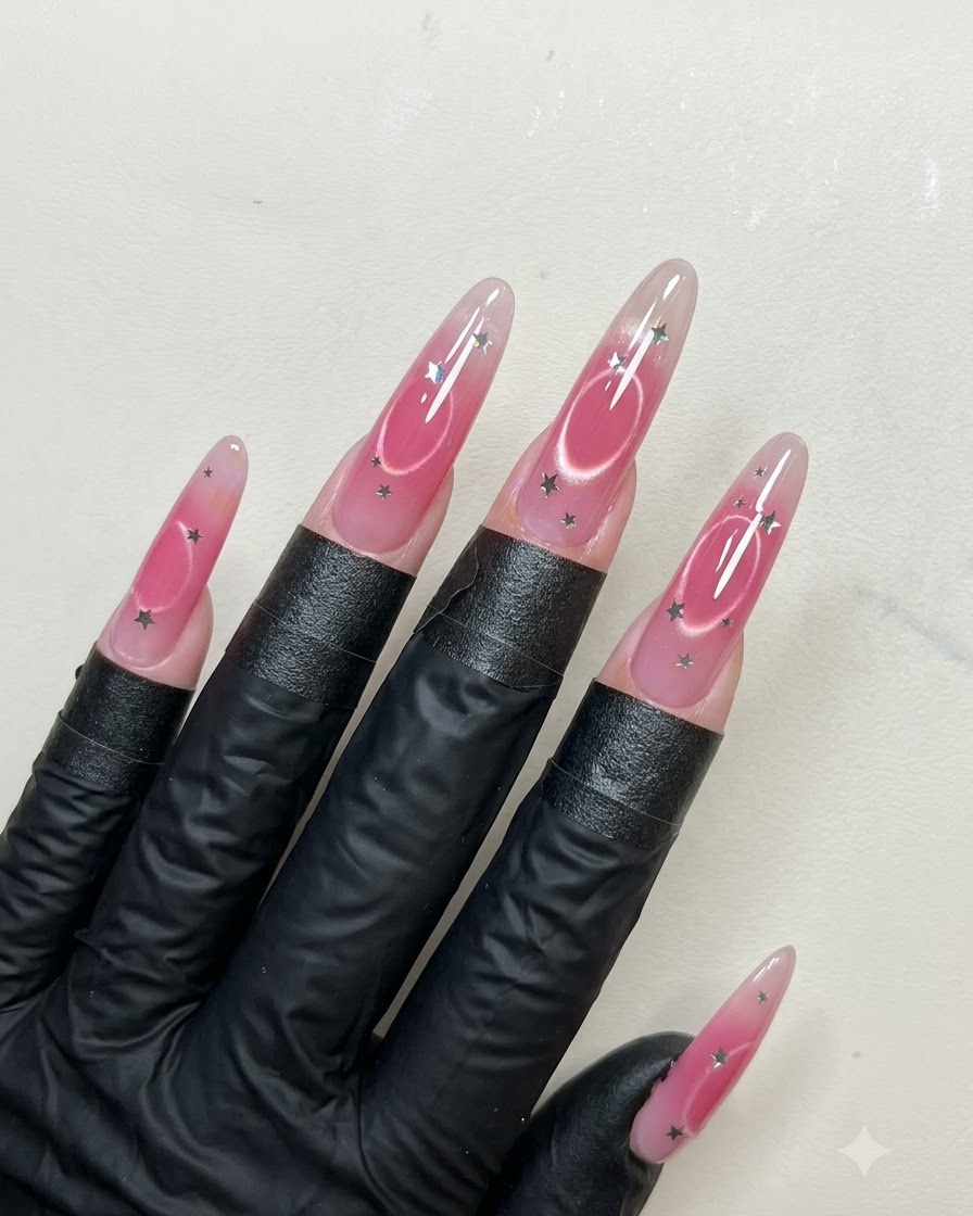 Un pincel de uñas aplicando una capa suave de capa superior brillante sobre uñas largas almendradas decoradas con lentejuelas de estrellas y arte de ojo de gato.
