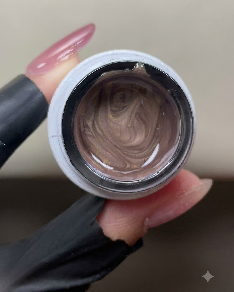 Un frasco abierto de gel ojo de gato rosa dorado brillante que muestra partículas magnéticas metálicas arremolinadas en su interior.