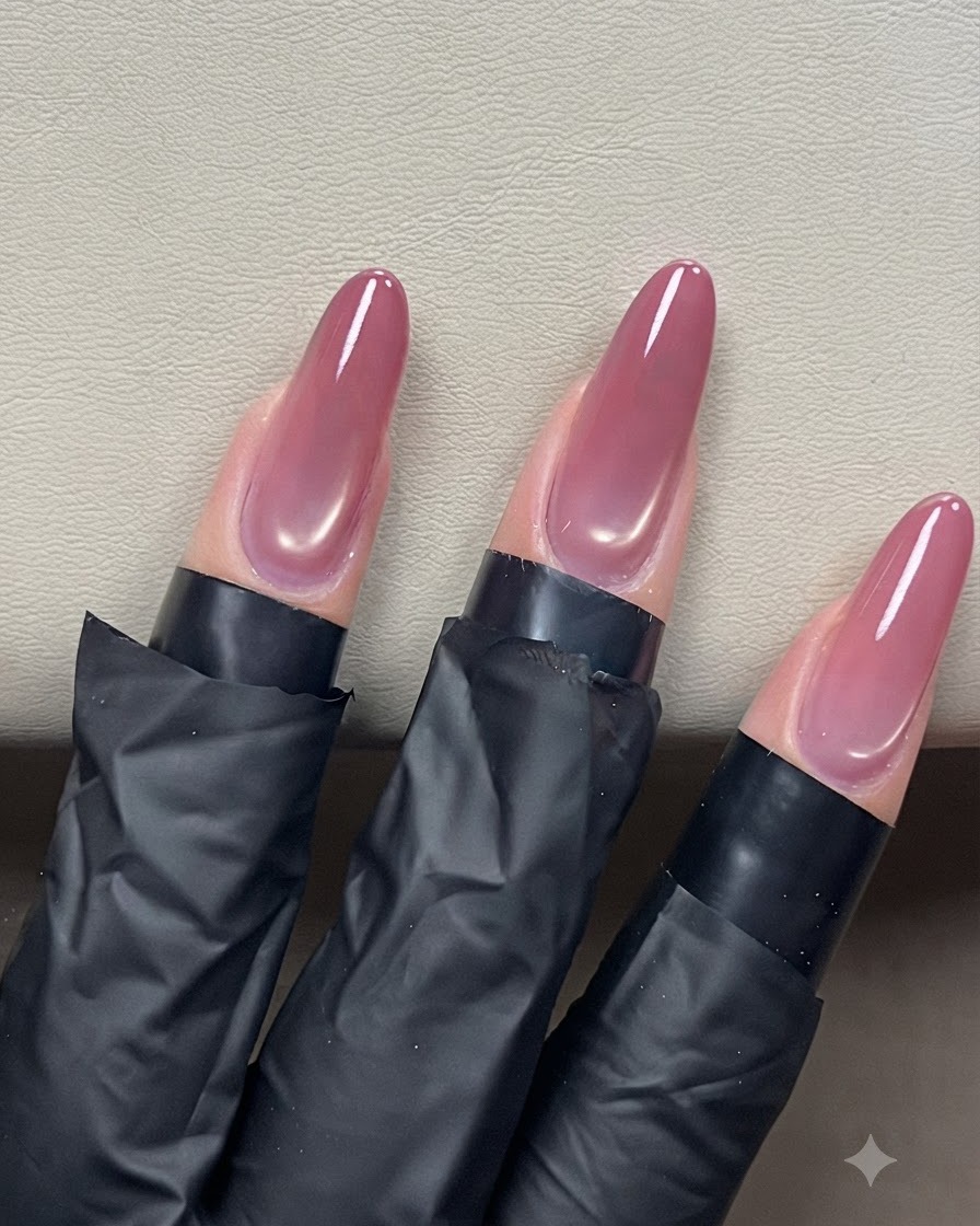 Un pincel de uñas deslizando una capa superior transparente sobre uñas almendradas de ojo de gato para un acabado brillante.