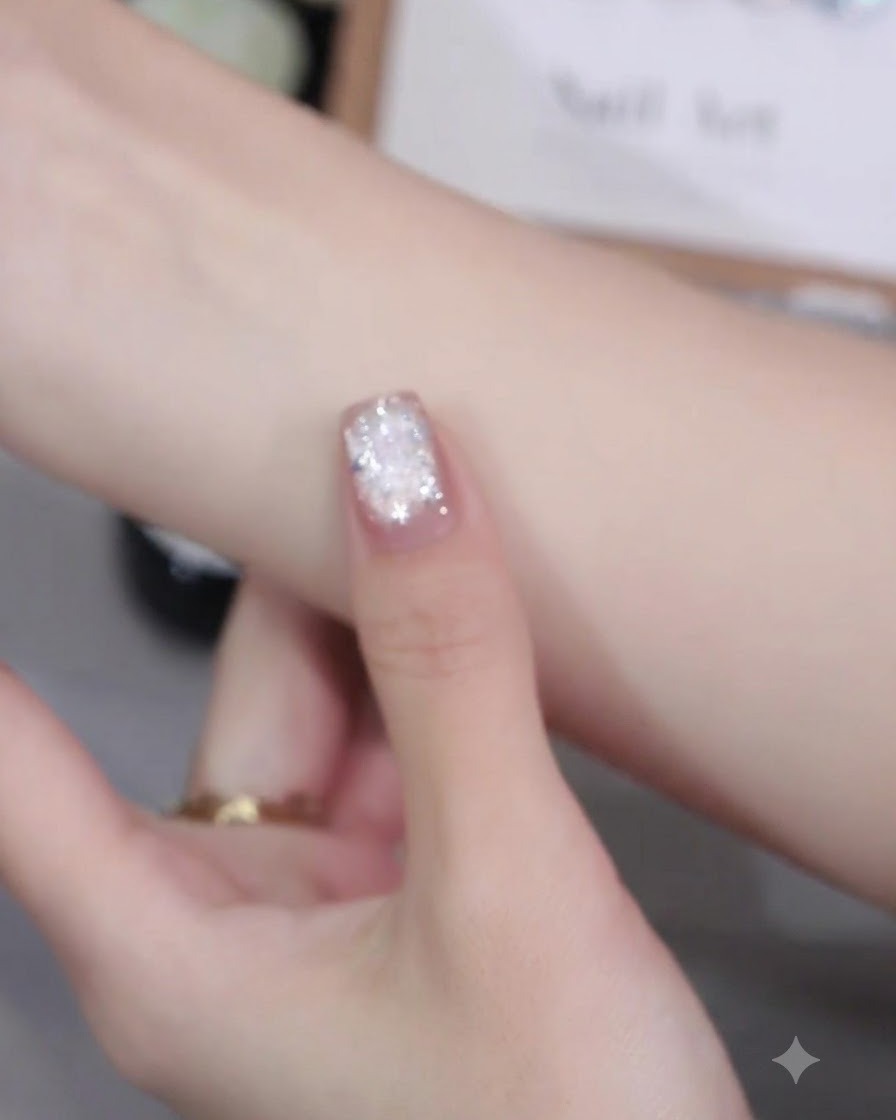 Un pincel de uñas aplicando esmalte en gel ojo de gato rosa de manera uniforme sobre la superficie de una uña.