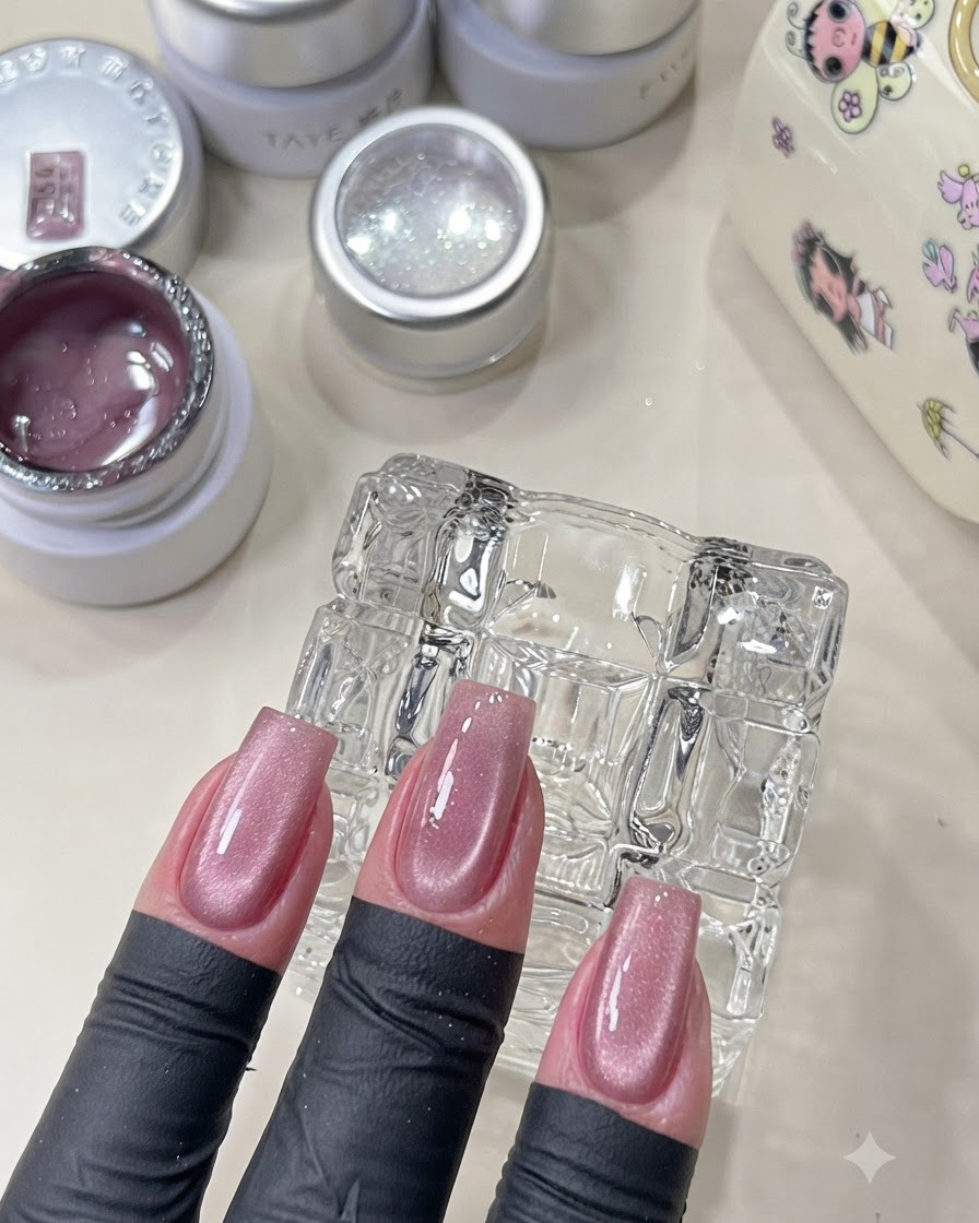 Una mano que muestra uñas rosadas de ojo de gato curadas con un acabado brillante.