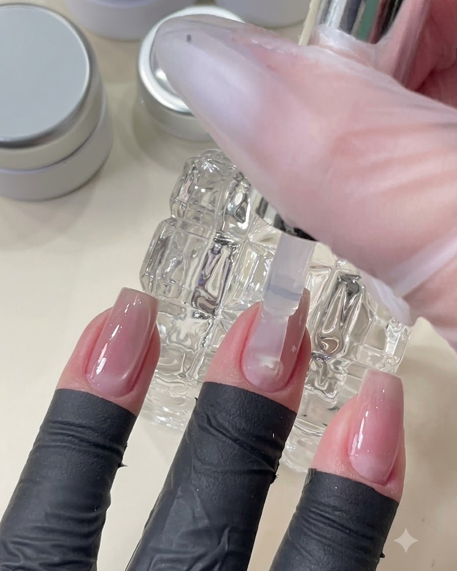 Un pincel aplicando una capa superior de gel transparente para alisar y nivelar la superficie de la uña sobre el arte de uñas incrustado.