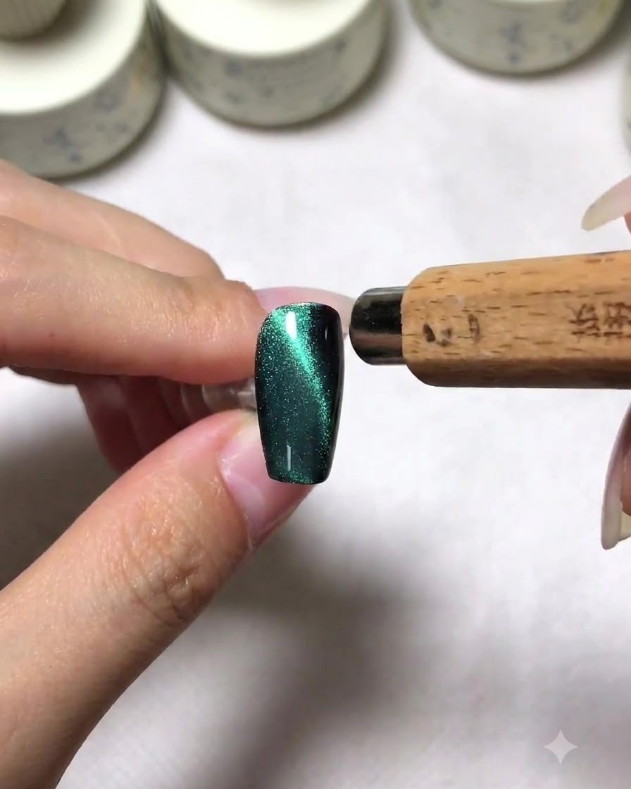 Una herramienta magnética posicionada en el lado derecho de una uña verde efecto ojo de gato para crear un destello lateral.