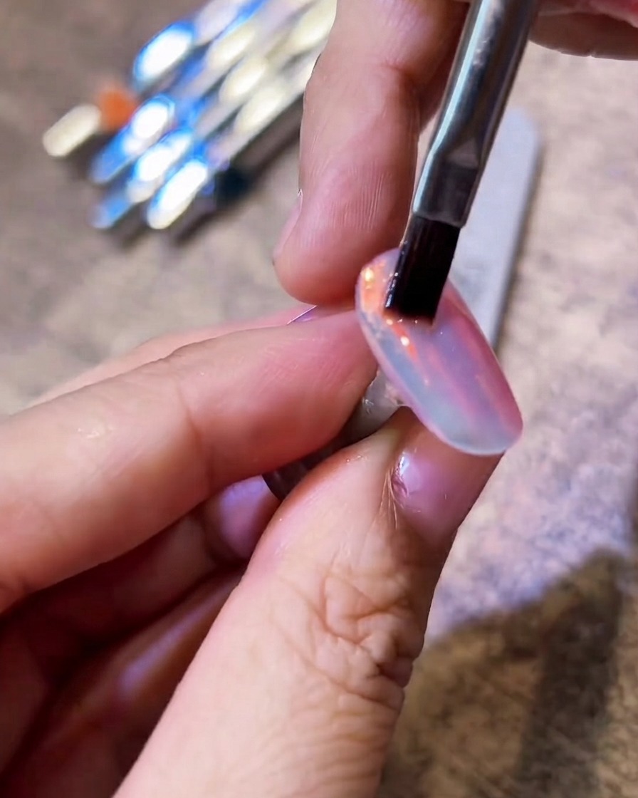 Pincel de cerdas planas barriendo suavemente una uña cromada para eliminar el exceso de polvo.