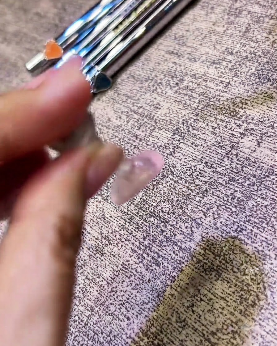 Pincel aplicando un top coat transparente sobre una uña con acabado cromado.