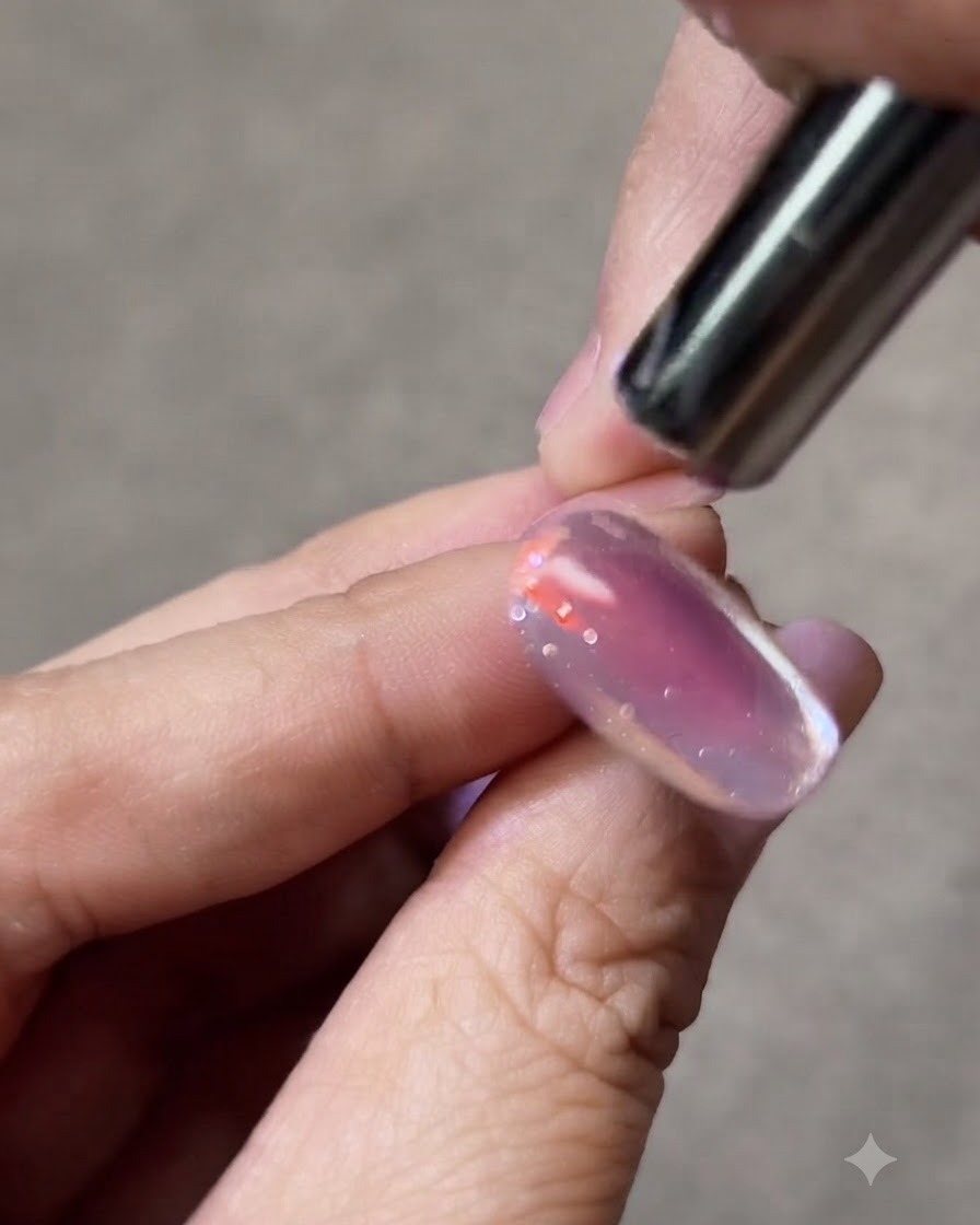 Imán pequeño sostenido cerca del lateral de una uña de gel para formar una franja de luz brillante.