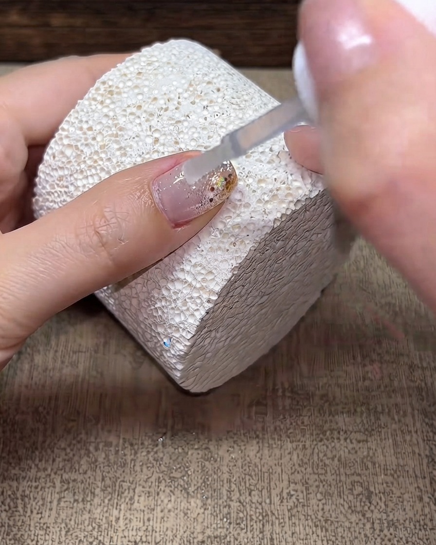 Un pincel aplicando una capa transparente de builder gel sobre una superficie de uña decorada.