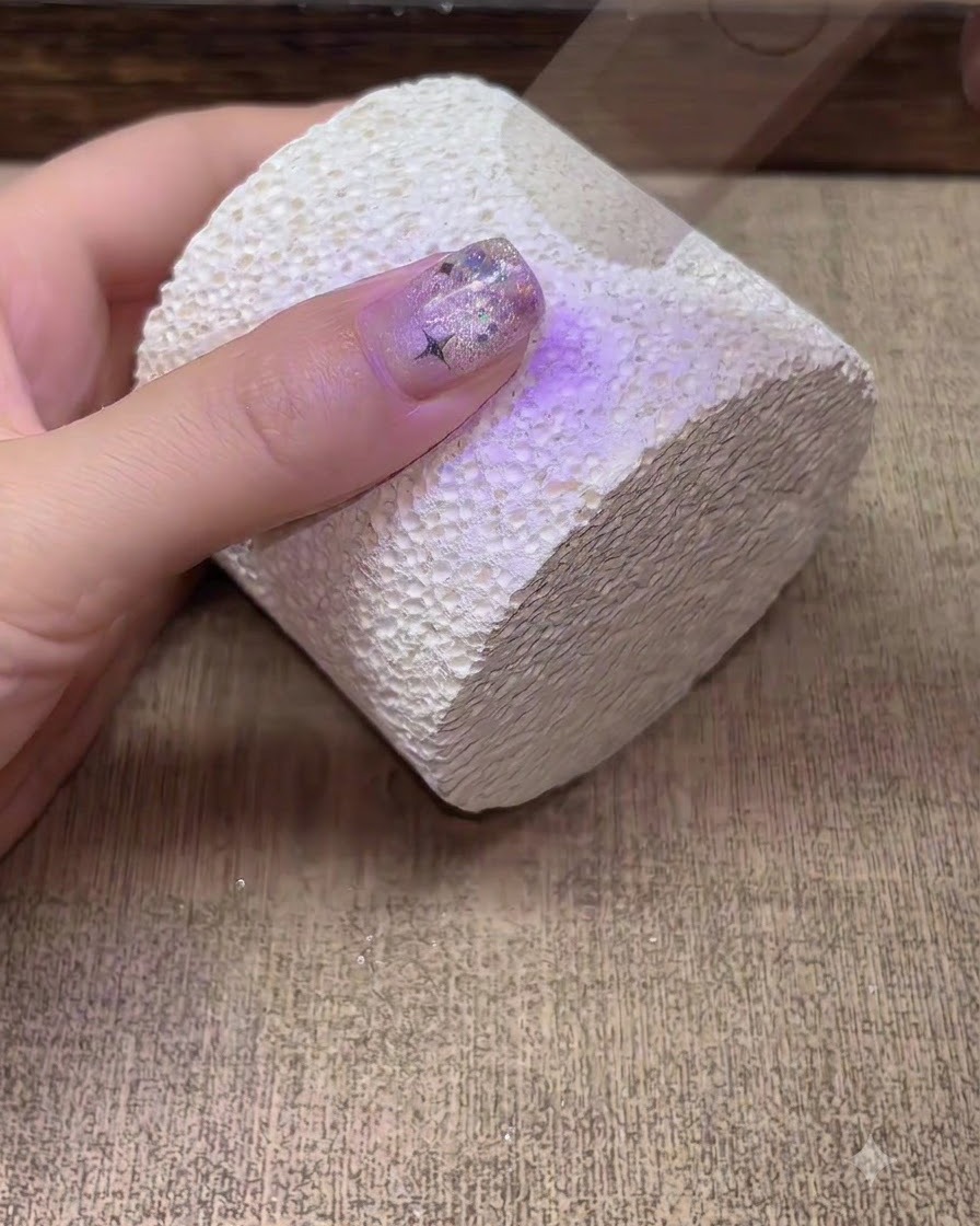 Una mano curándose bajo una lámpara de uñas UV LED de color púrpura.